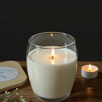Bougie blanche allumée dans un verre transparent près d’une petite bougie sur une table en bois